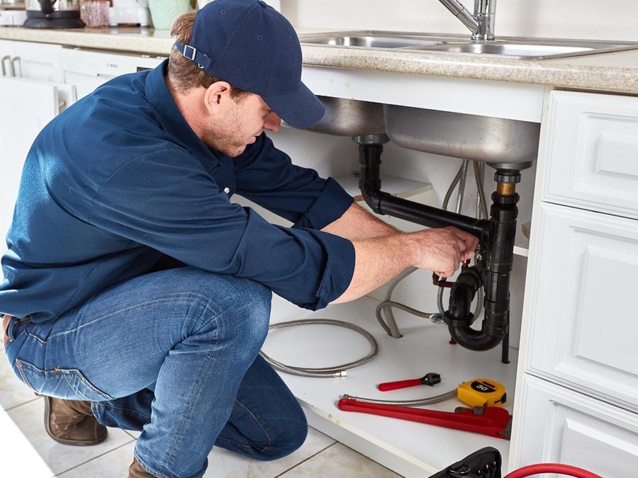 Plumber repairing pipes under a kitchen sink