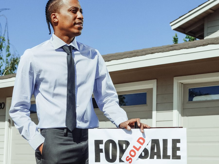 Real estate agent standing beside a For Sale sign with a Sold sticker